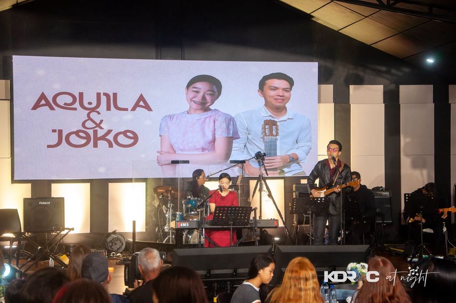 Duo performing on the lit stage beside a screen with their names
