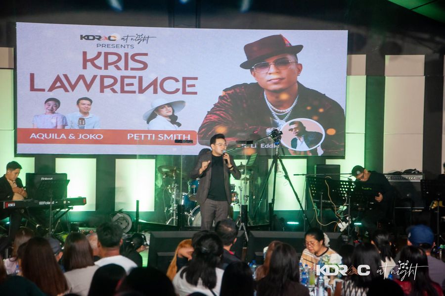Singer and band on the stage in front of the Kris Lawrence screen